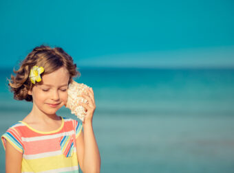 dziewczynka nad morzem ćwiczy percepcję słuchową wsłuchując się w muszlę